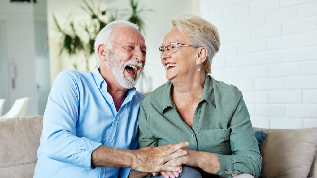 Szczęśliwi seniorzy śmieją się na kanapie, ciesząc się ze świadczenia z ZUS