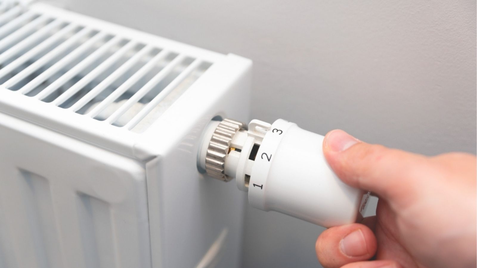 Dłoń regulująca pokrętło termostatu na białym kaloryferze w mieszkaniu