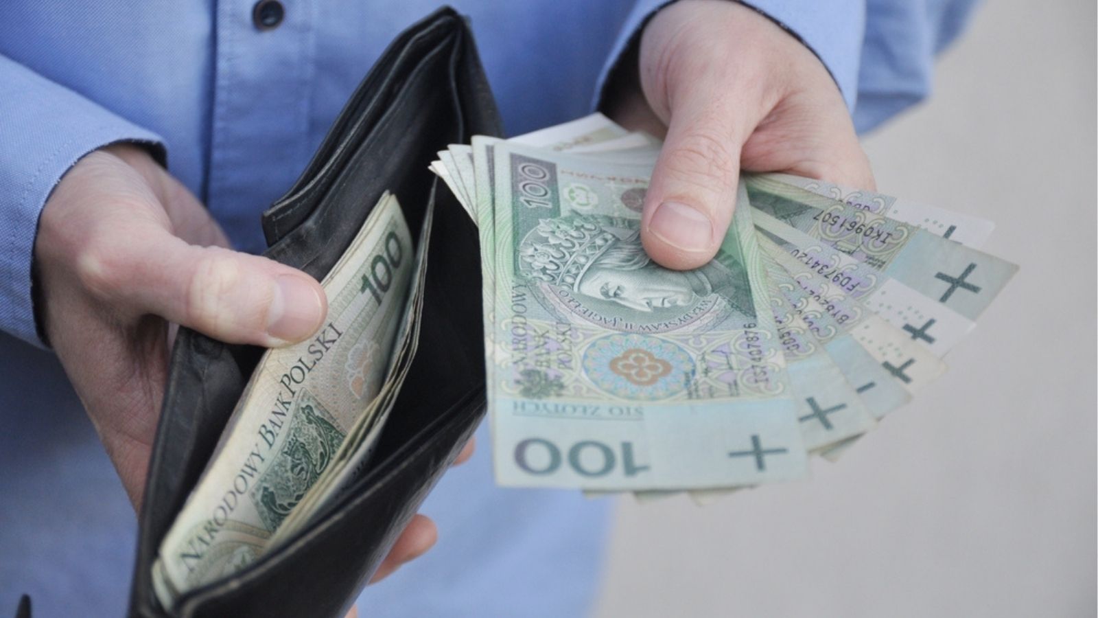 Dłonie wyciągające polskie banknoty ze skórzanego portfela