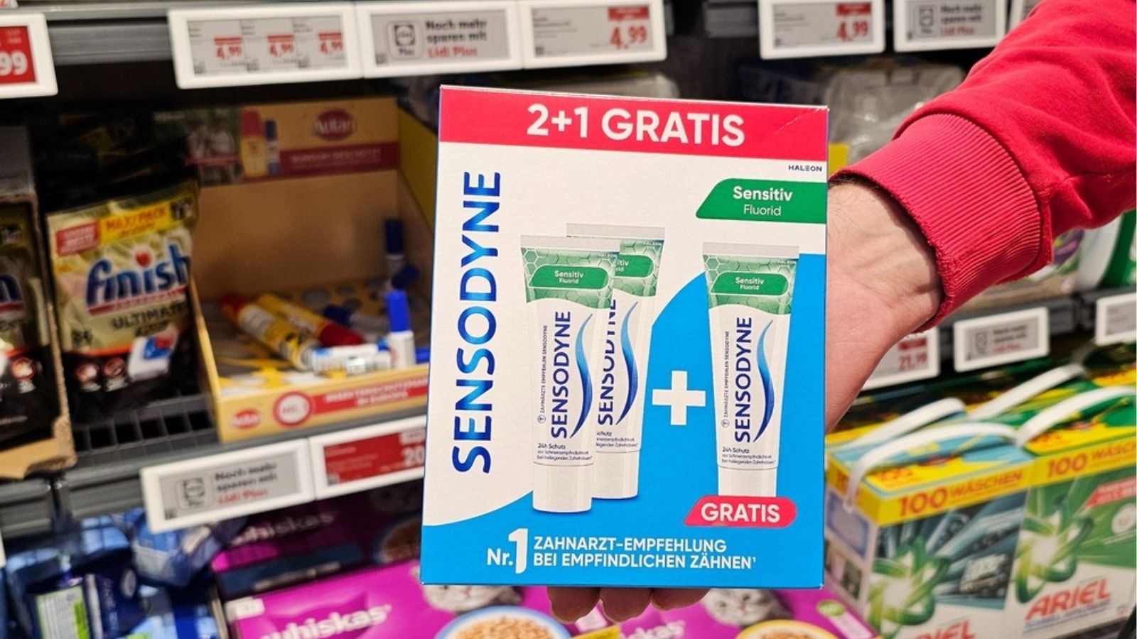 Klientka w sklepie trzyma trzy produkty i sprawdza ich ceny na półce